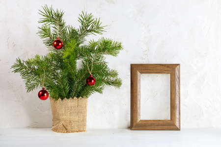 Trendy Christmas minimal image with fir branches bouquet as alternative Xmas tree and empty wooden frame for photo on white background. Holiday decorations. Copy space. Mock up.の写真素材