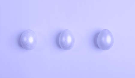 Three glossy Easter eggs are lying in row. Creative minimal festive Easter background. Trendy toning in color of year lavender Very Peri. View from above. Flat lay, copy space.の写真素材
