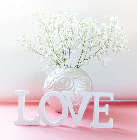 White letters LOVE with round vase of white gypsophila flowers on pink-white. Creative holiday greeting card for Valentine's day, Mother's day, March 8th or Birthday. close up.の写真素材