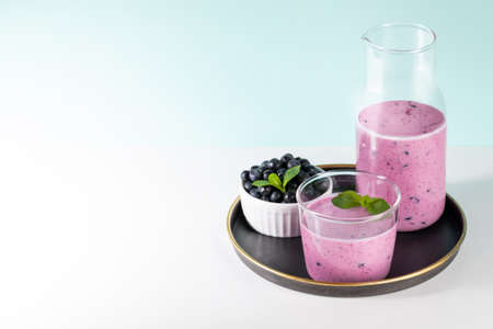 Glass and bottle of blueberries smoothie, blueberries bowl with mint on round plate on turquoise backdrop. Healthy drink is antiviral, useful for immunity. You can also use vegetable milk. copyspace.の写真素材