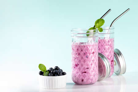 Two glasses of blueberries smoothie with straws, blueberries bowl on white-turquoise backdrop. Healthy drink is antiviral, useful for immunity, reducing sugar, excess weight, depression. copyspace.の写真素材