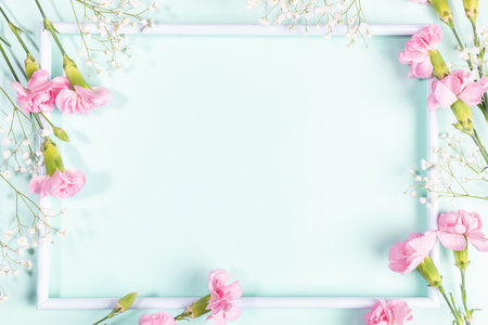 Empty white frame with gentle pink carnations and white gypsophila flowers on it on pastel light blue backdrop. Happy Mother's or Valentine's day. view from above. copyspace. holiday mockup.の写真素材