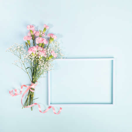 Mock up empty frame, bouquet of gentle pink carnation and gypsophila flowers, decorated with ribbon on light blue background. Happy Mother's or Valentine's day. Top view, copy space.の写真素材
