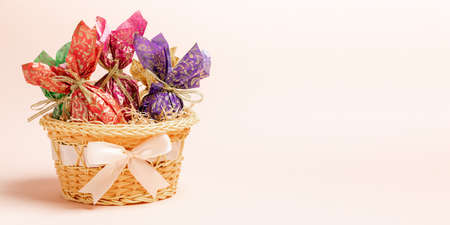 Easter decorative eggs wrapped in color paper with golden ribbons in basket decorated by bow. Pastel...