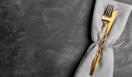 Golden cutlery fork and knife in gray napkin on dark gray shabby background. Mock up for cooking recipe or text. concept of eating. Banner. view from above. close up. copyspace.の写真素材
