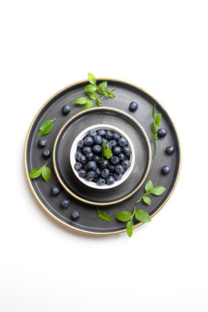 White bowl with washed wild blueberries and green leaves laid out on metallic plates on white. Blueberry - superfood rich in vitamins useful for health. copyspace. top view. vertical orientation.の写真素材
