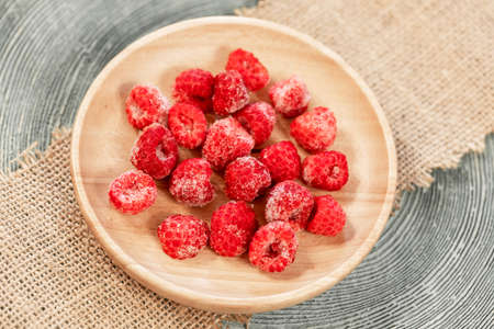 Frozen raspberry on wooden plate on burlap napkin. wooden backdrop. Frozen berries are healthy treat in winter because they retains all vitamins. view from above. horizontal orientation.の写真素材