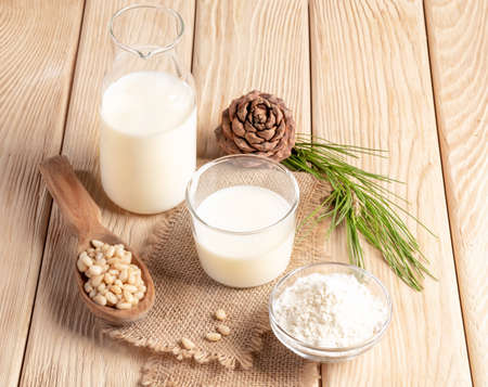 Still life of healthy organic cedar products - milk in glass and bottle, flour and nuts on burlap napkin on wooden table. Plant based non dairy alternative milk. natural milk replacer. top view.の写真素材
