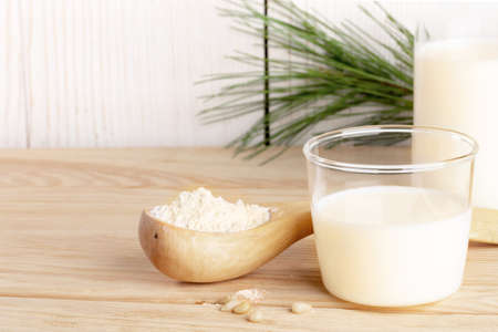 Organic milk replacer. Small glass with cedar milk and flour in wooden spoon for its cooking on wooden table close up. Plant based alternative milk. lactose free drink. copyspace. selective focus.の写真素材