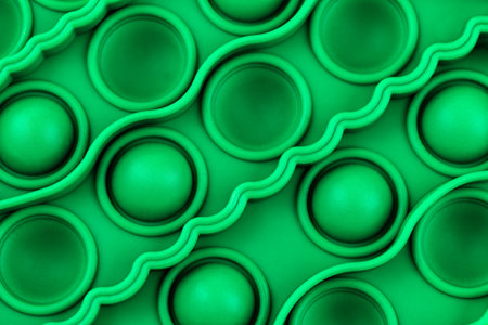 Relief surface of green silicon anti stress sensory pop toy with bumps and pits close up. Popular...