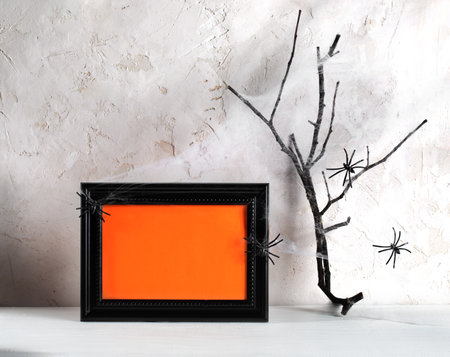 Halloween minimal image. Black frame with orange empty space for text, spiders, dry twig in cobwebs on white wooden table on neutral backdrop. Holiday card or party invitation. Mockの写真素材