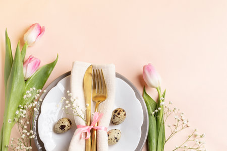 Quail eggs, golden cutlery in napkin on plates, pink tulips and gypsophila on light peach...
