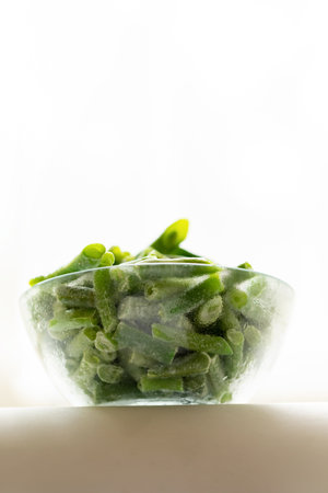 Bottom view to glass bowl with frozen green beans on white background. Frozen vegetables. Healthy...
