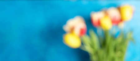Defocused image with colorful tulips bouquet on bright blue background. Blooming season. Template. Banner. Blurred spring background with copy space.の写真素材