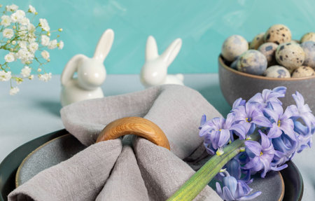 Close up Easter table serving. Gray napkin with hyacinth flower on gray plates, quail eggs, ceramic...