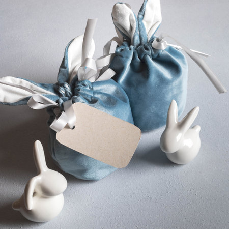 Easter card. Two creative gift bags with bunny ears and white small ceramic bunnies on gray...