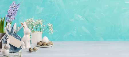 Easter still life of holiday decorations on turquoise. Eggs of natural colors, ceramic bunnies,...