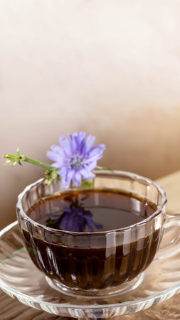 Close up figured glass cup with chicory tea and flower on beige background. Chicory tea is prebiotic, good for sleep. Herbal medicine for human health. Vertical orientation. Copy space. Mockup.の写真素材