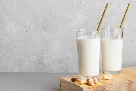 Brazil nut milk is served in two clear glasses with bamboo straws, placed on a wooden surface, surrounded by scattered nuts, creating a natural and inviting atmosphere for healthy livingの写真素材