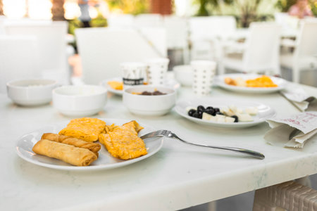 Breakfast spread includes savory pastries, cheese, olives, and fruits arranged on a marble table, surrounded by a bright outdoor atmosphere, inviting a relaxed dining experienceの写真素材