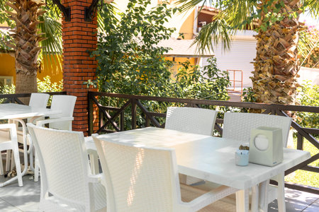 Outdoor dining space featuring white wicker furniture, surrounded by vibrant greenery and palm trees, creating a serene atmosphere for relaxation and enjoyment in a tropical settingの写真素材