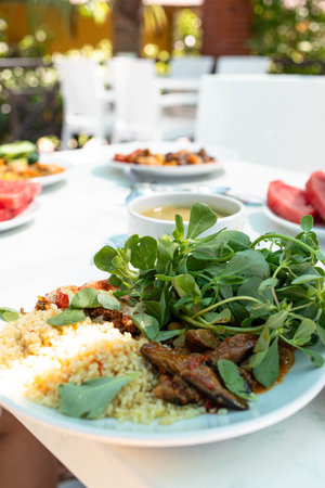 Freshly prepared plate featuring couscous, vibrant greens, and grilled meat, beautifully arranged outdoors with a lively atmosphere, showcasing a delicious culinary experience and inviting presentationの写真素材
