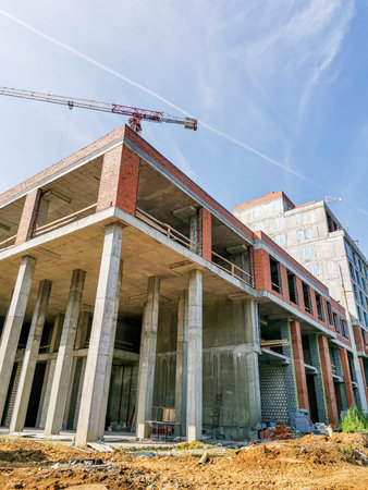 Construction site featuring a modern building framework with exposed concrete pillars and a crane...