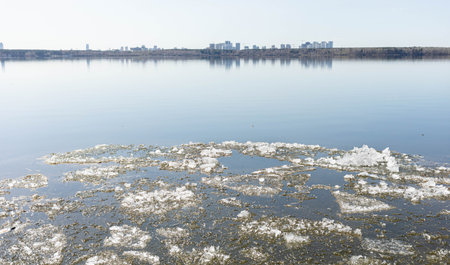 Tranquil lake scene featuring floating ice fragments on the surface, reflecting a distant skyline under a clear blue sky, creating a serene and peaceful atmosphere in natureの写真素材