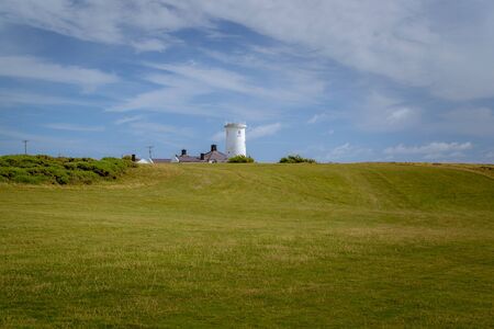 The coast of Wales with a historic lighthouse among green meadows.の写真素材