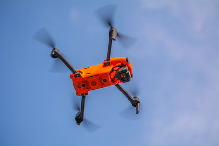 Orange drone flying in the blue sky with white clouds on a sunny day