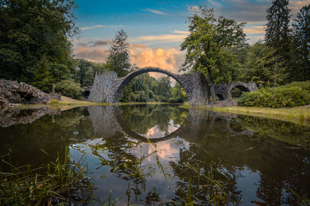 Old stone bridge over the lake in the park on a summer eveningの写真素材