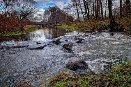 Autumn landscape with a small river and a bridge in the background