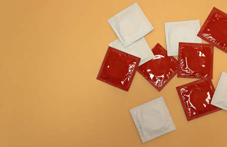 Several unopened red and white condoms on orange background, concept of sexual prophylaxiの写真素材
