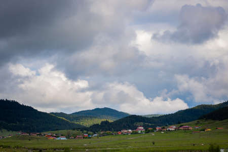 a village near the forest covered hills with cloudy skyの写真素材