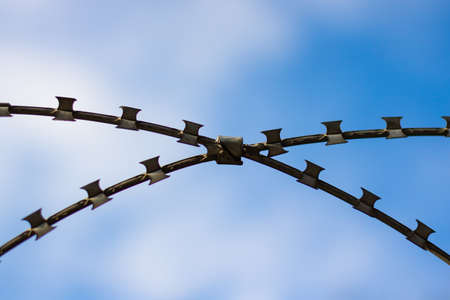 x shape razor wire fence against blue sky. Barbed wire concept. security background photo.の写真素材