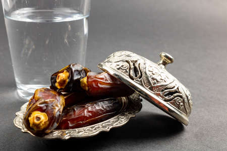 dates on the bowl and a glass of water on gray background. High quality photo. Ramadan foods and snacks. Iftar party. Fasting in Ramadan.の写真素材