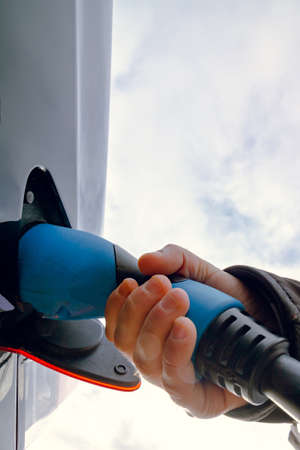 Man holding an attached charger on the Electric Vehicle in focus. High quality photo. Charging EV...