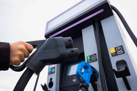 Man holding a EV charger. EV Charger station on the background. EV charger station background....
