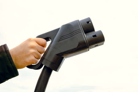 Man holding a EV charger against the cloudy sky. Copy Space. EV charger. Electric vehicle charging....