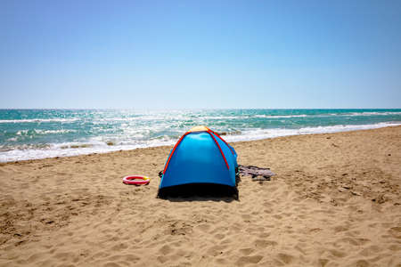 A blue tent on the beach. Camping near the sea. Camping in summer. Sea, sun and sand tourism. No people.の写真素材