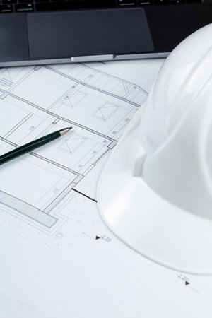 A pen, a white safety helmet and a laptop on the architectural plan. Engineering, architecture,...