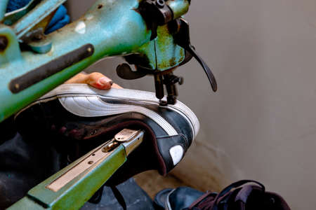 Sneakers repair. Shoemaker repairs a sneaker on sewing machine. selective focus. Noise included.の写真素材