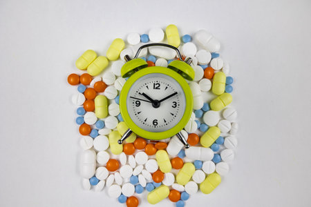 Daily medicine routine concept photo. Pills and a clock isolated on white background.