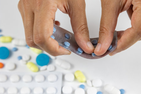 Woman removing blue pills from plastic blister. Recovery from sickness concept photo. Various pills or tablets on the background. Selective focus on the hands.の写真素材
