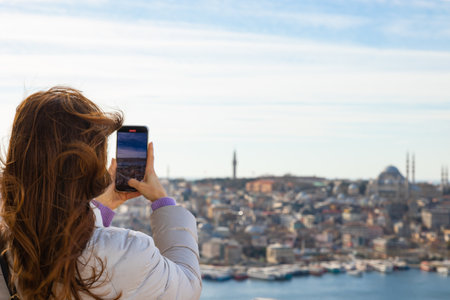 Travel to Istanbul background photo with copy space for text. A woman taking photo of Istanbul with her mobile phone on Galata Tower. Suleymaniye Mosque and Eminonu district on background.の写真素材