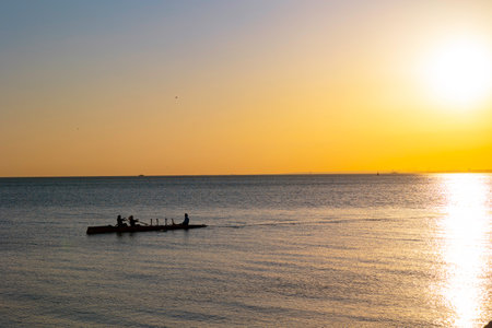 Silhouettes of athletes canoeing at sunset over the calm sea. Athletes paddling their canoes across the sea.の写真素材
