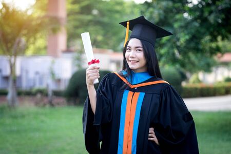 Portrait of happy and excited of young Asian female university graduate wears graduation gown and...