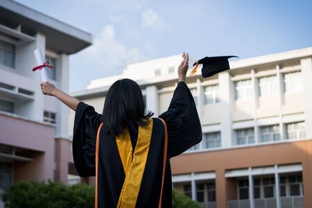 Portrait of happy and excited of young Asian female university graduate wears graduation gown and hat celebrates with degree in university campus in the commencement day. Education concept.の写真素材