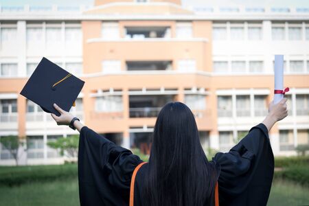 Portrait of happy and excited of young Asian female university graduate wears graduation gown and hat celebrates with degree in university campus in the commencement day. Education concept.の写真素材