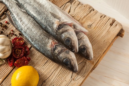 Sea bass fish with garlic, rosemary, tomatos and lemon on a wood table from aboveの写真素材